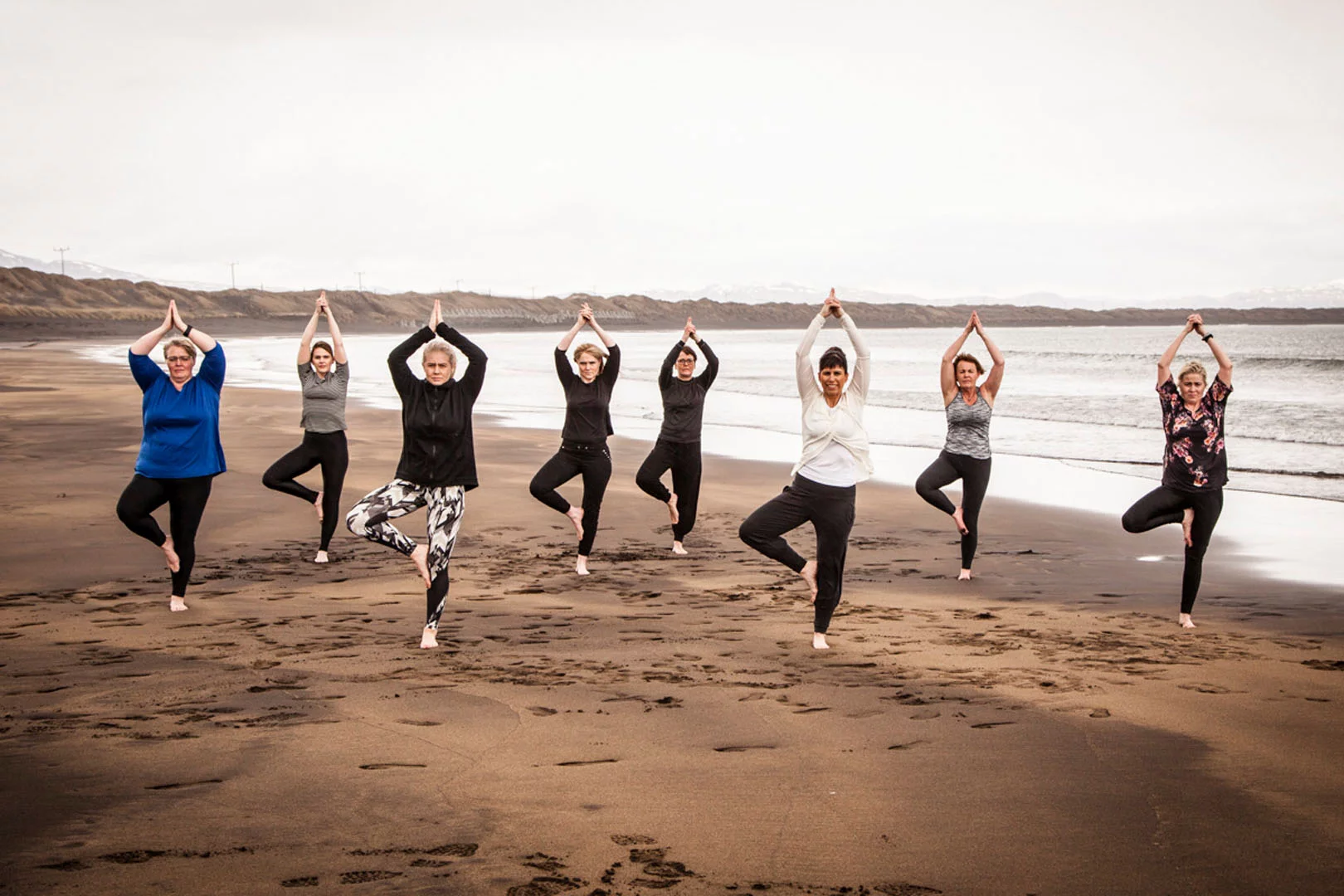 A group on women does a yoga pose on the black beach in Þorlákshöfn